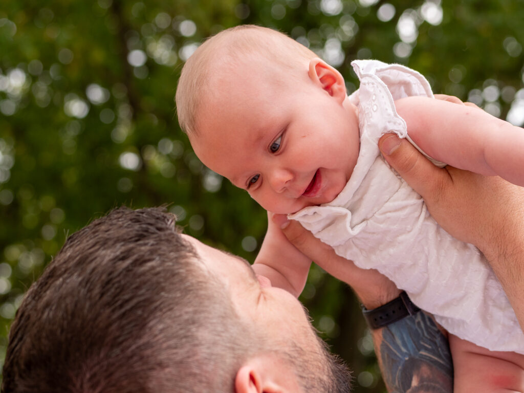 Vater hält sein Baby liebevoll in die Höhe bei einem Familienfotoshooting draußen in Bonn