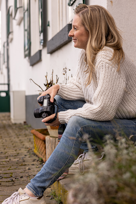 Fotografin aus Bonn mit Kamera in der Hand wird lächelnd von der Seite auf einer Teffenstufe fotografiert