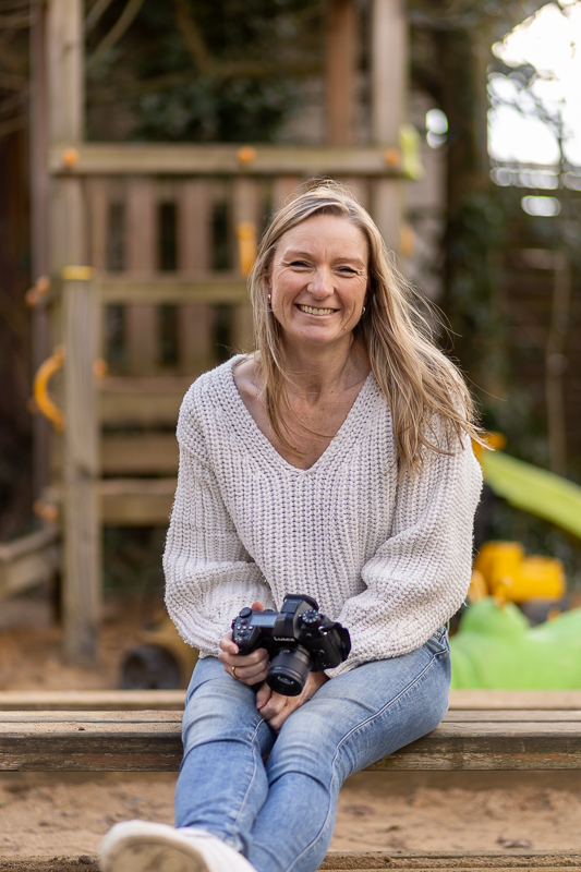 Sympathische Fotografin aus Bonn für Baby-, Familien- und Kitafotografie sitzt lachend mit Kamera auf einem Spielplatz