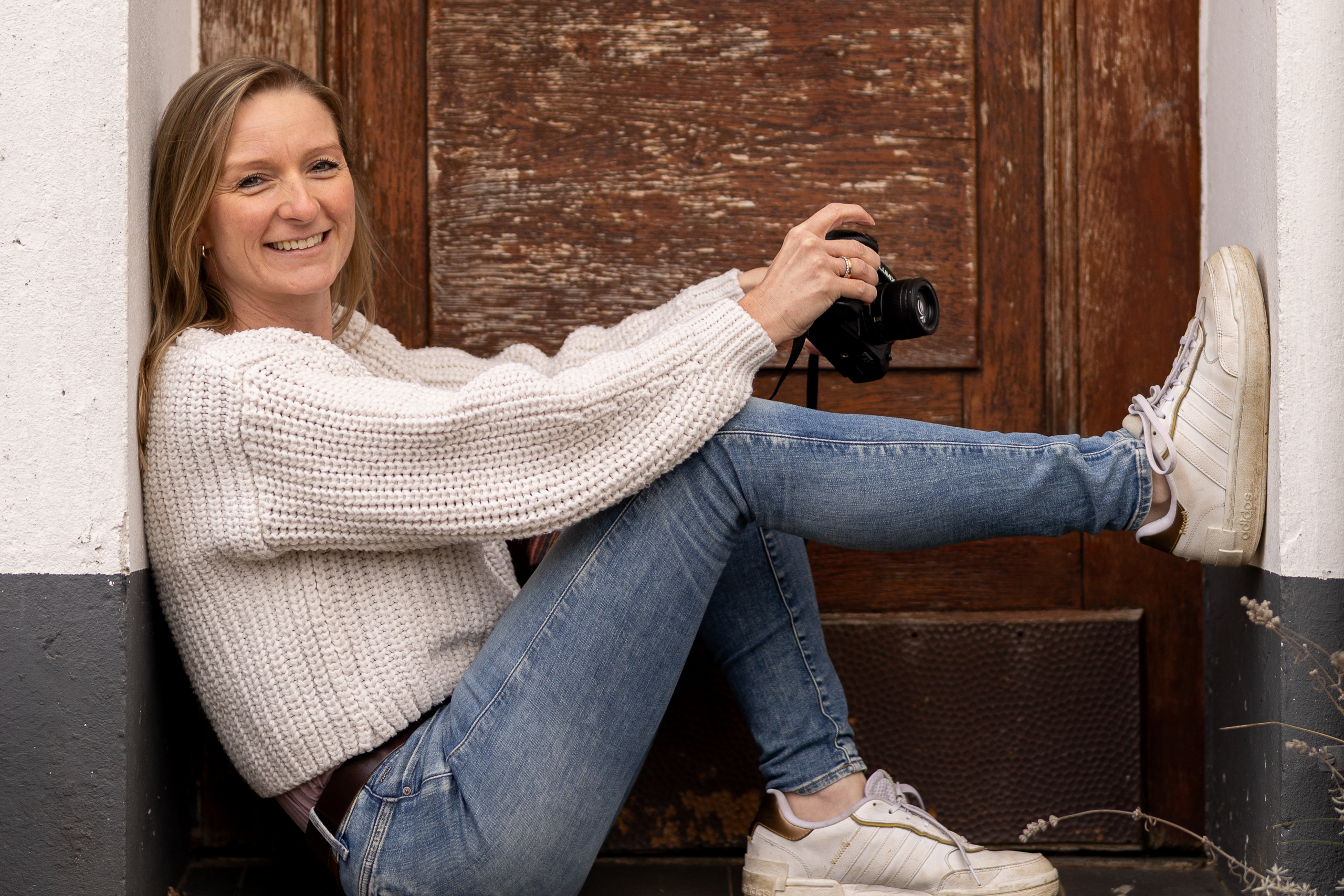 Sympathische Fotografin aus Bonn für Baby-, Familien- und Kitafotografie mit Kamera in der Hand lacht direkt in die Kamera bei einem natürlichen Portrait