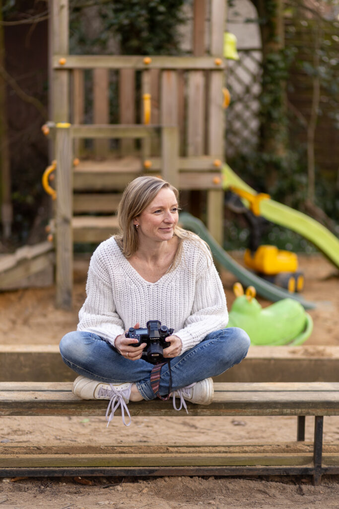 Kitafotografin aus Bonn sitzt entspannt vor einem Klettergerüst auf einem Spielplatz mit Kamera