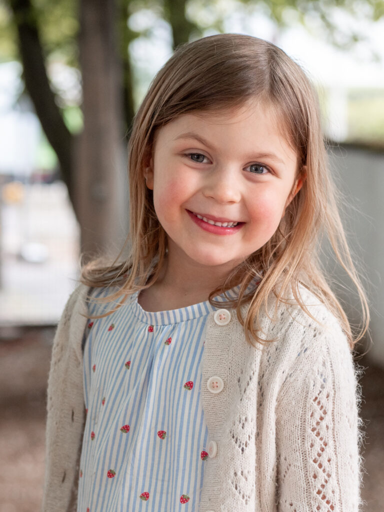 Nätürliches Kinderportait, bei dem das Mädchen direkt in die Kamera lächelt.