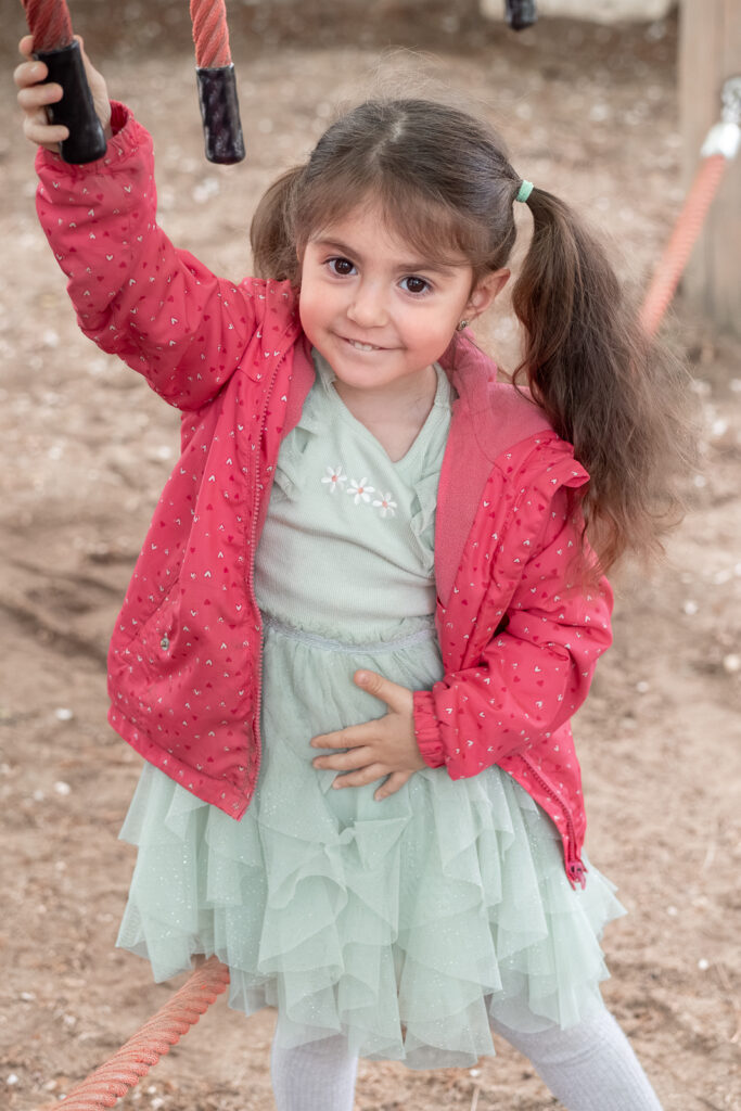 Mädchen im hübschen Kleid spielt lächelnd an einem Seil auf dem Spielplatz.